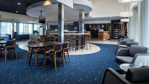 A modern hotel lobby with a central bar area, seating arrangements, and a reception desk. - Courtyard by Marriott Phoenix Airport (Phoenix)