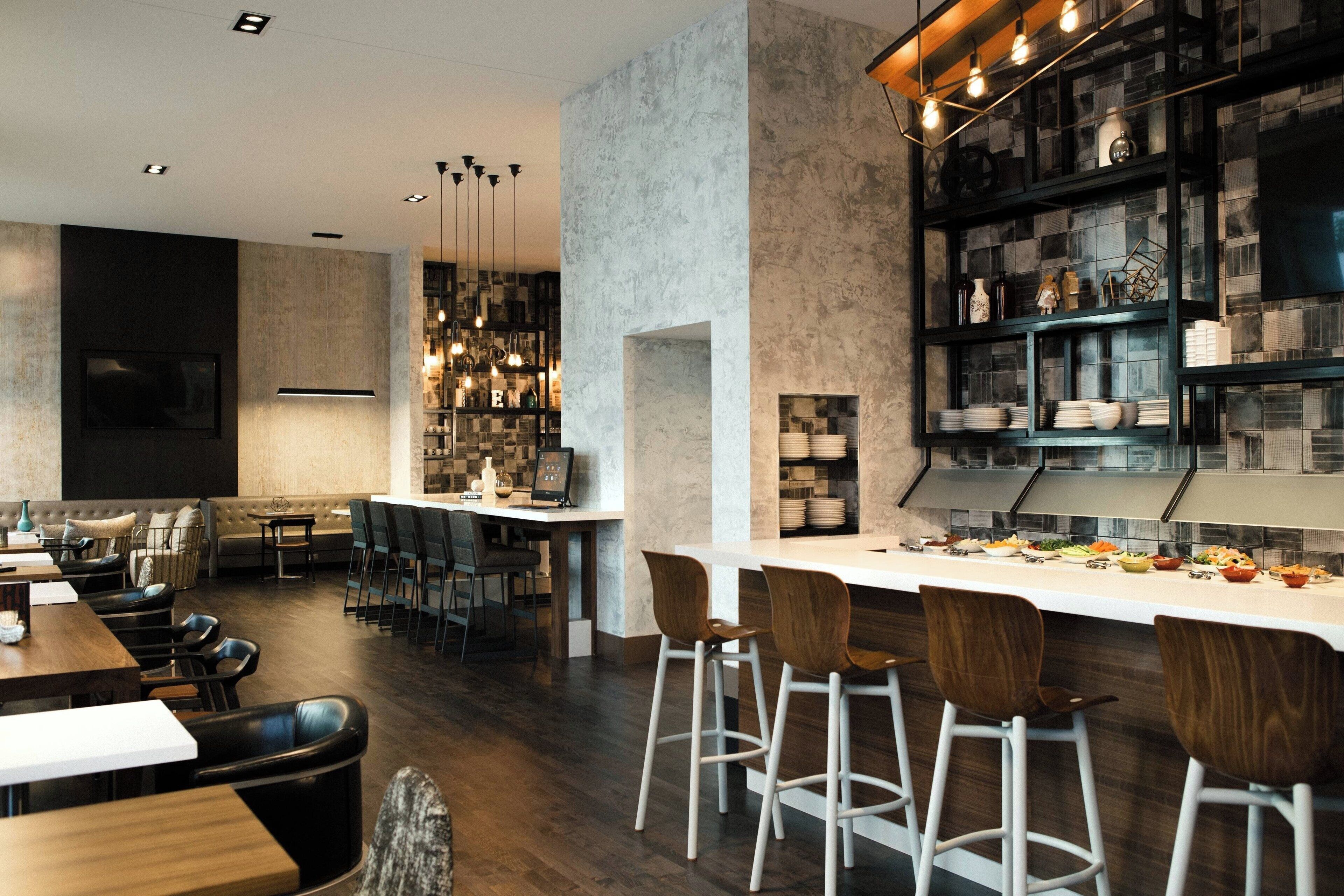 Restaurante moderno com área de bar, cadeiras altas e diversos pratos expostos em prateleiras.