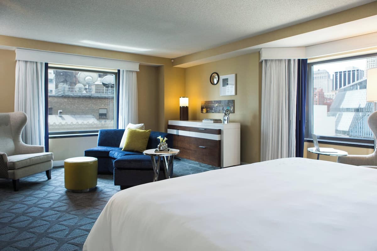 Une chambre d’hôtel avec un grand lit, un canapé, un bureau et une vue sur la ville par les fenêtres.