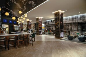A modern bar area with wooden flooring, bar stools, hanging pendant lights, and a large screen displaying content.