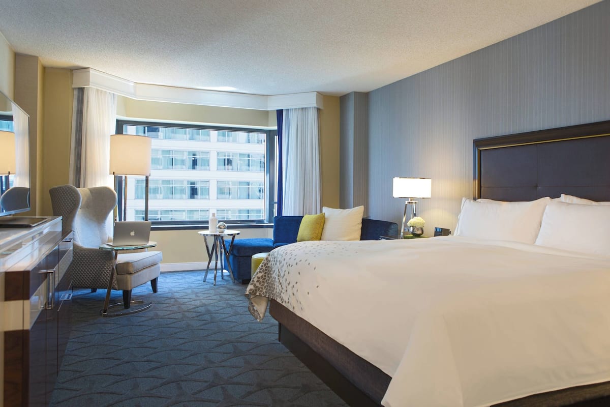 Une chambre d’hôtel avec un grand lit, un bureau avec un ordinateur portable, une chaise et une petite table avec une lampe.