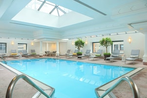 Una piscina interior con tragaluces, sillones de descanso y plantas en macetas.