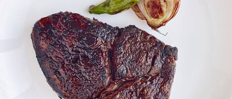A steak with a side of roasted vegetables and a green chili on a white plate.
