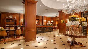 A lobby with a reception desk, a large chandelier, a marble floor, and wooden paneling.