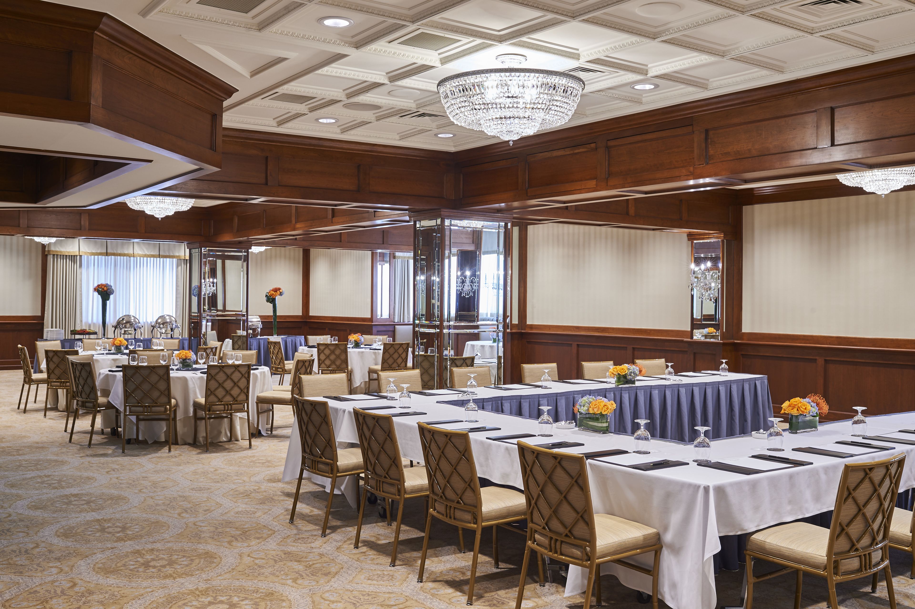 A large conference room with multiple tables and chairs, a chandelier, and a carpeted floor.