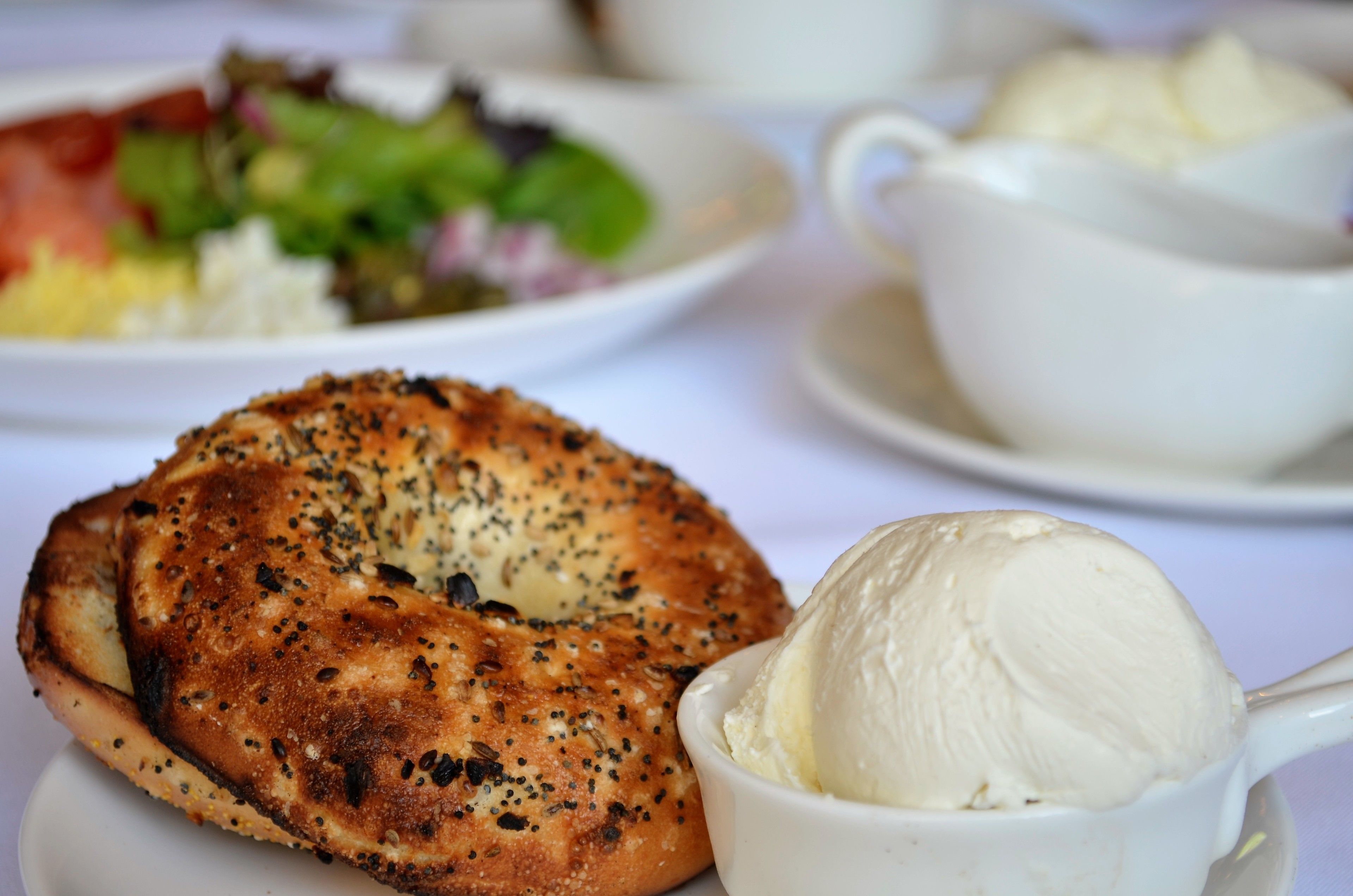 Un desayuno con un bagel, una porción de helado y una taza de café sobre una mesa blanca.