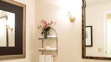 A bathroom with a toilet, sink, and two mirrors. There is a towel rack with a towel and a vase with flowers.