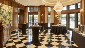 A lobby with a checkered floor, wooden paneling, a large chandelier, and tables set up for a meeting or event.