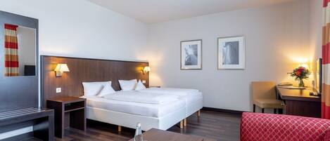 A hotel room with a bed, bedside tables, a desk, a chair, and a red sofa.