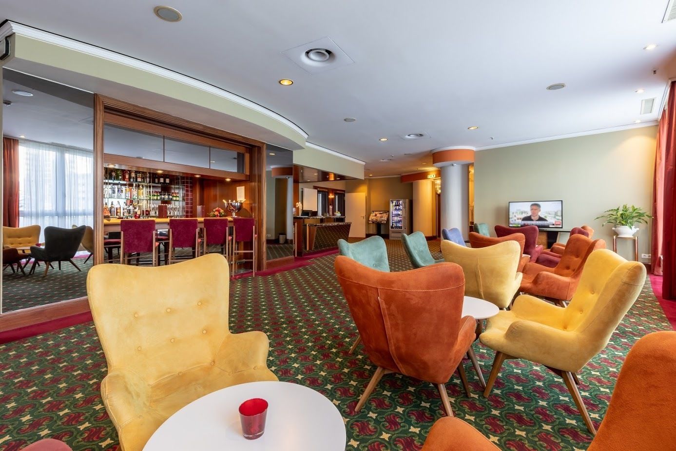 Un hall de hotel con zona de bar, diversas opciones de asientos y una pantalla de televisión.