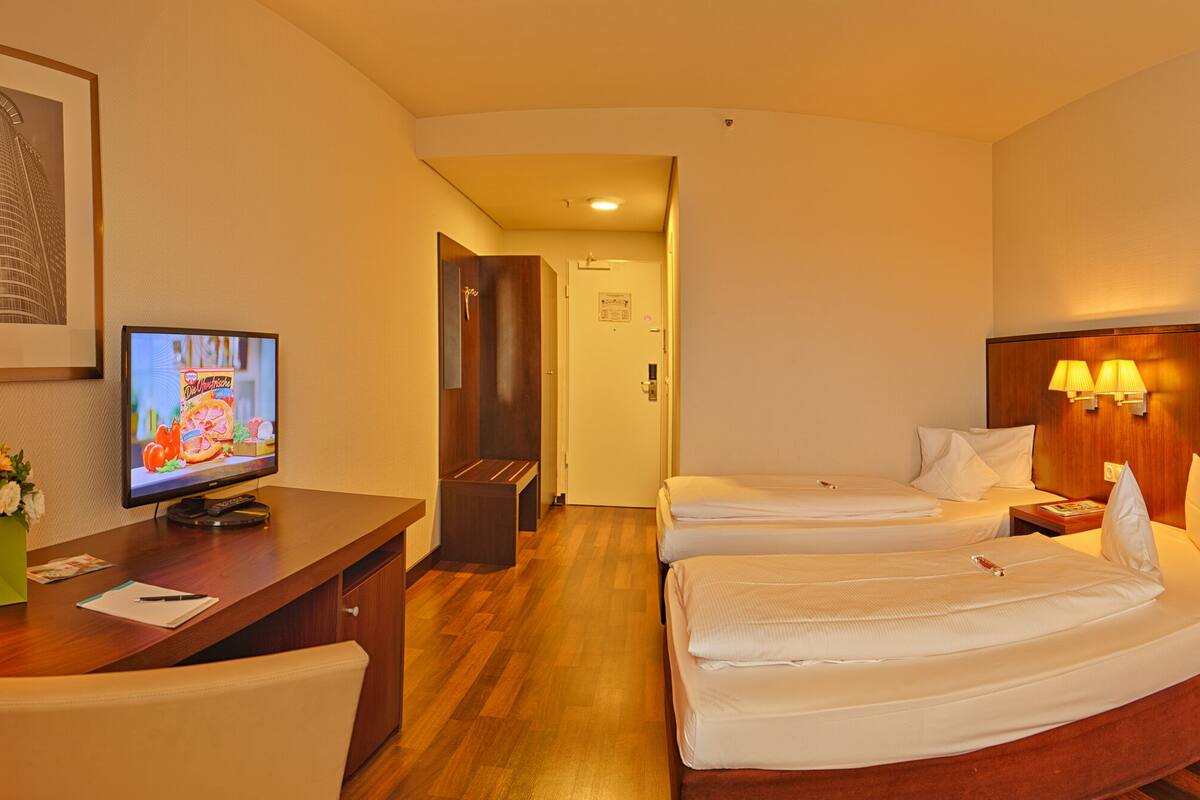 A hotel room with two beds, a desk with a telephone, a television, and a red chair.