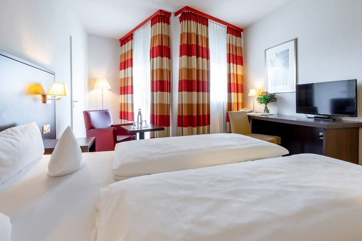 A hotel room with two beds, a desk, a chair, a TV, and curtains.