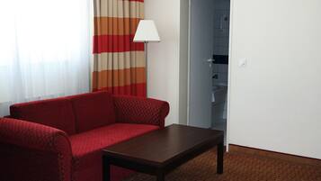 Una habitación con un sofá rojo, una mesita de madera, una lámpara y una puerta que da a un baño.