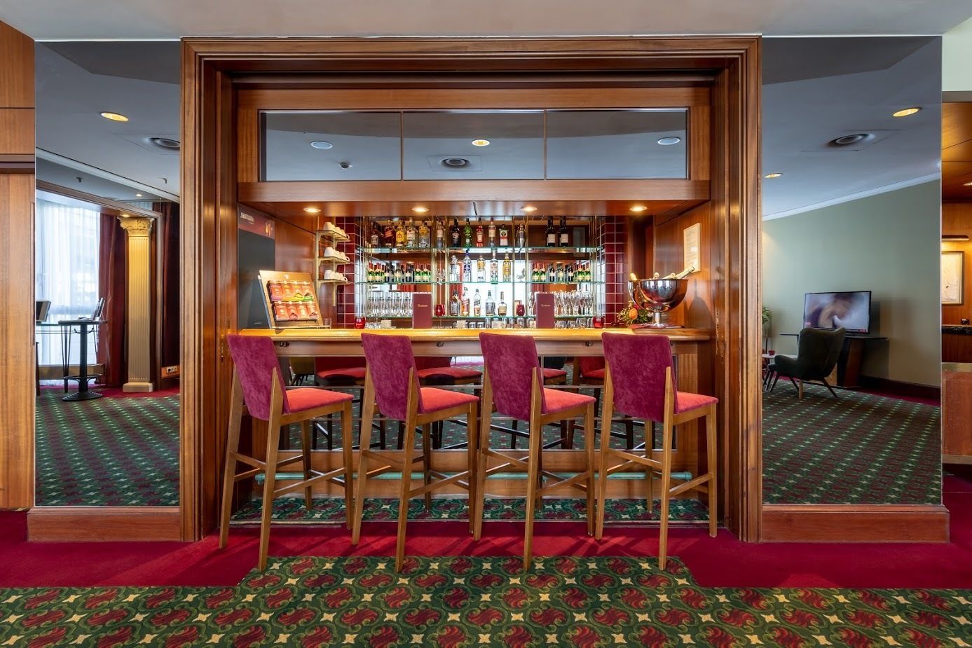 A bar area with a wooden counter, multiple bar stools, and a variety of bottles and glasses.