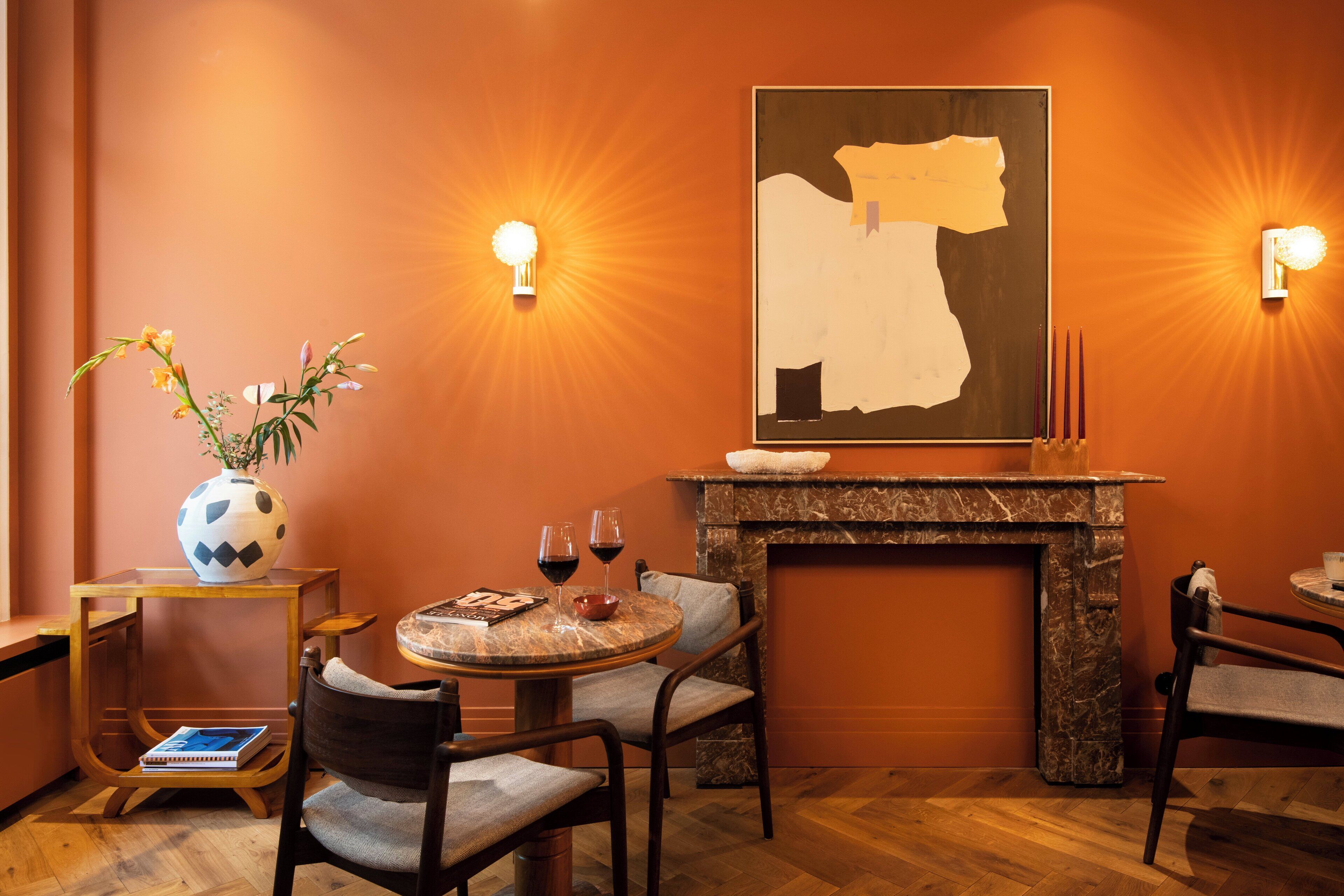 Una habitación acogedora con chimenea, una mesa redonda con sillas, un jarrón con flores y dos lámparas de pared.