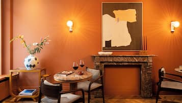 Una habitación acogedora con chimenea, una mesa redonda con sillas, un jarrón con flores y dos lámparas de pared.
