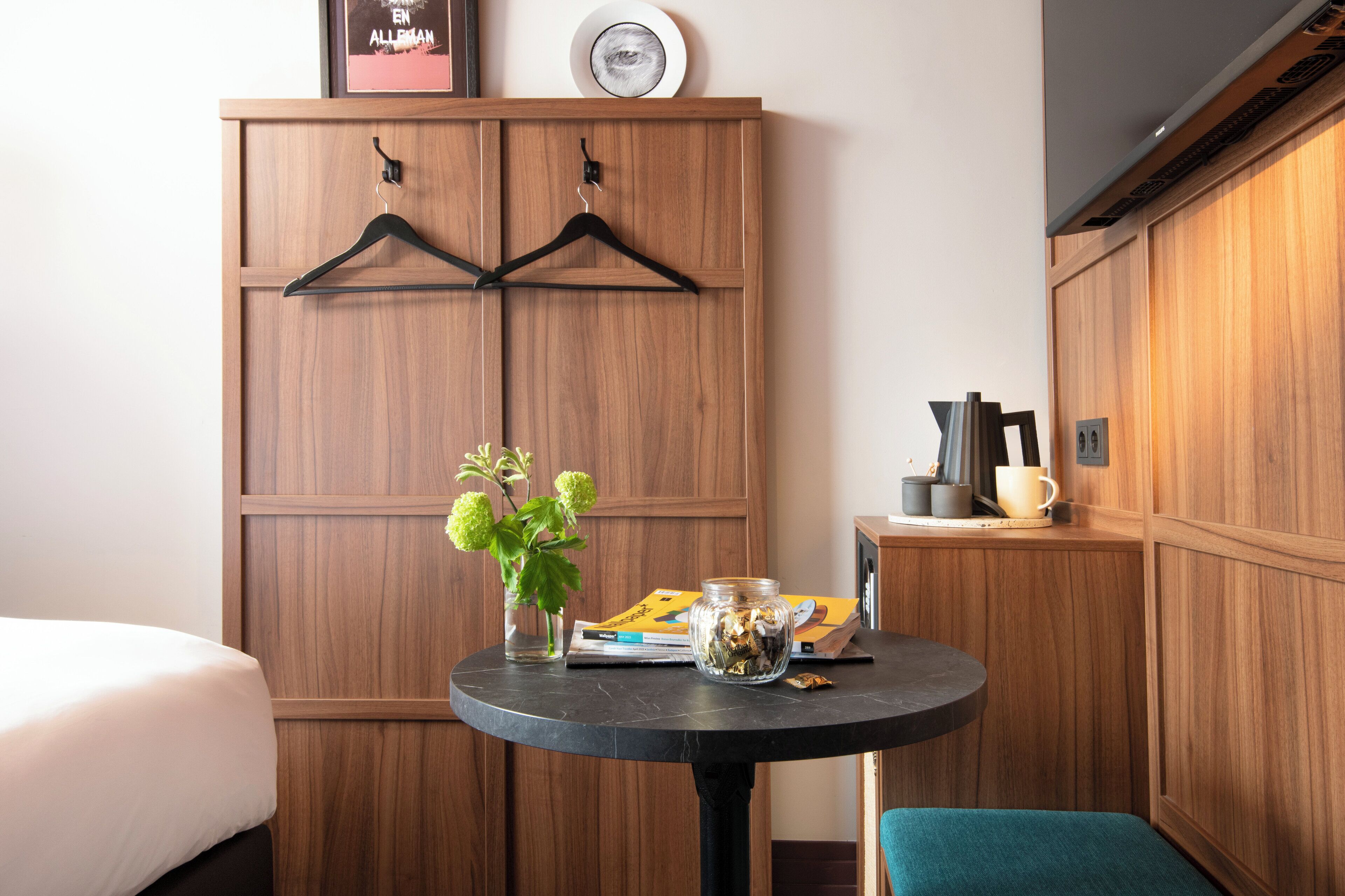Une chambre d’hôtel avec une armoire en bois, une table ronde ornée d’un vase de fleurs et un lit avec une literie blanche.