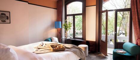 A hotel room with a large bed, a side table with a lamp, a window with curtains, and a view of the outside.