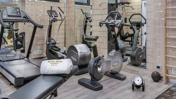 A gym with various exercise equipment, a bench, and a wall-mounted rack.