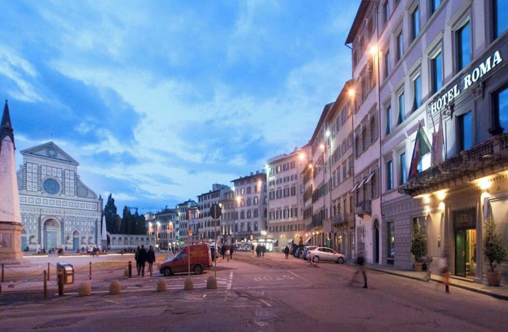 A city street with historic buildings, a prominent church, and a hotel named 'HOTEL ROMA' on the right.