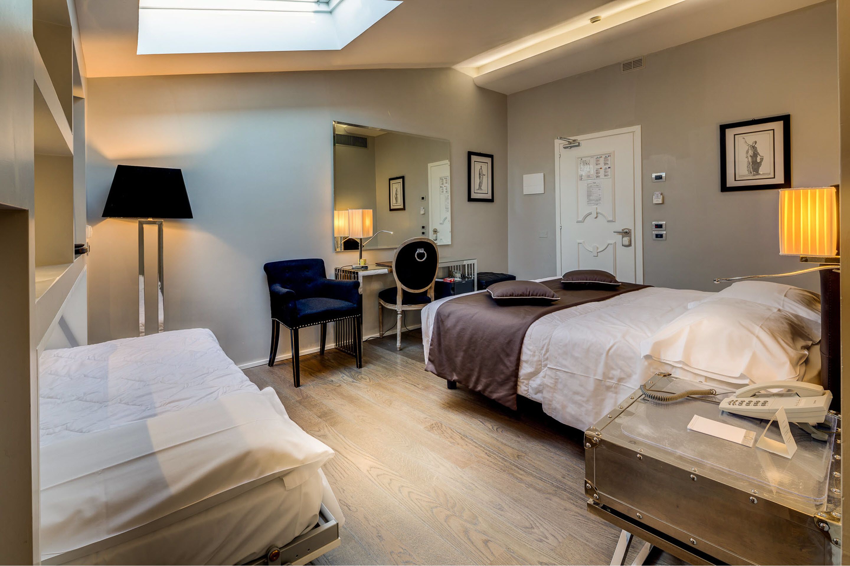 A hotel room with two beds, a desk, a chair, a lamp, and a suitcase with a phone on it.