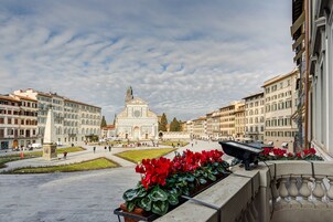 Una piazza con un monumento al centro, circondata da edifici neoclassici e un'aiuola fiorita.