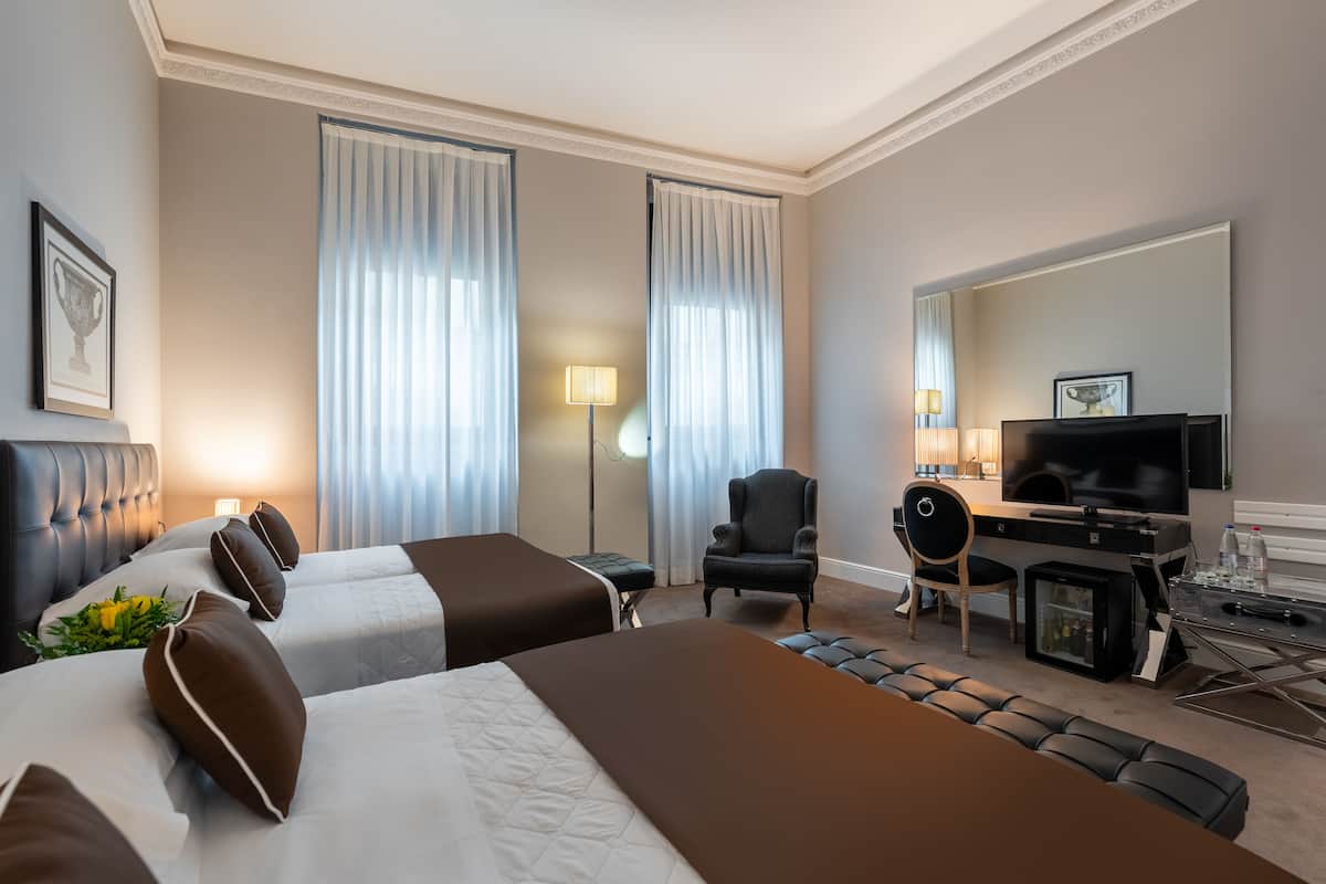 A hotel room with two beds, a desk with a television, and a seating area with a chair and ottoman.