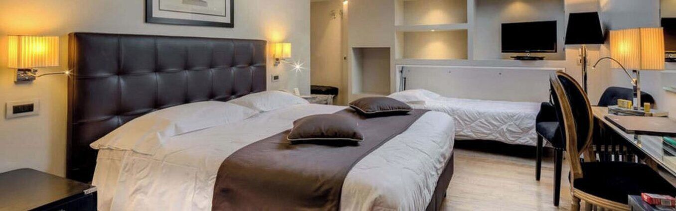 Een hotelkamer met een groot bed, een kleiner bed, een bureau met stoel, een televisie en een lamp.