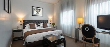A hotel room with a bed, a desk, a chair, a television, and a window with curtains.