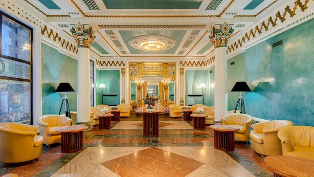 A luxurious lobby with a grand chandelier, ornate ceiling, and plush seating areas.