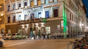 A multi-story hotel with a classic architectural style, featuring a prominent sign reading "HOTEL ROMA" and a flag.