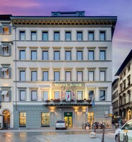 Un hotel a più piani con una facciata classica, un cartello ben visibile con su scritto "HOTEL ROMA" e un ingresso a livello strada con una porta verde.
