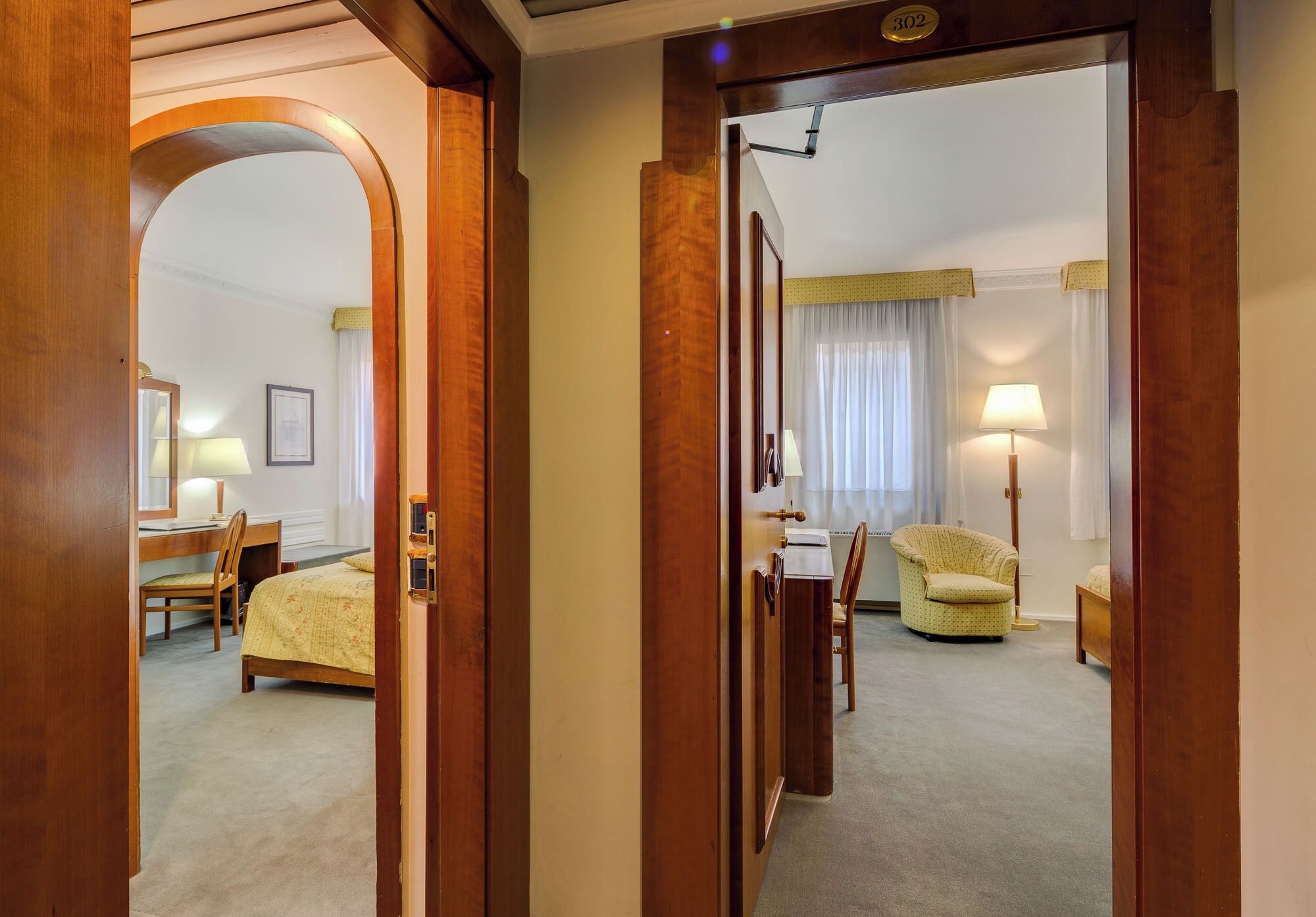A hotel room with a bed, a desk, a chair, a lamp, and a window with curtains.