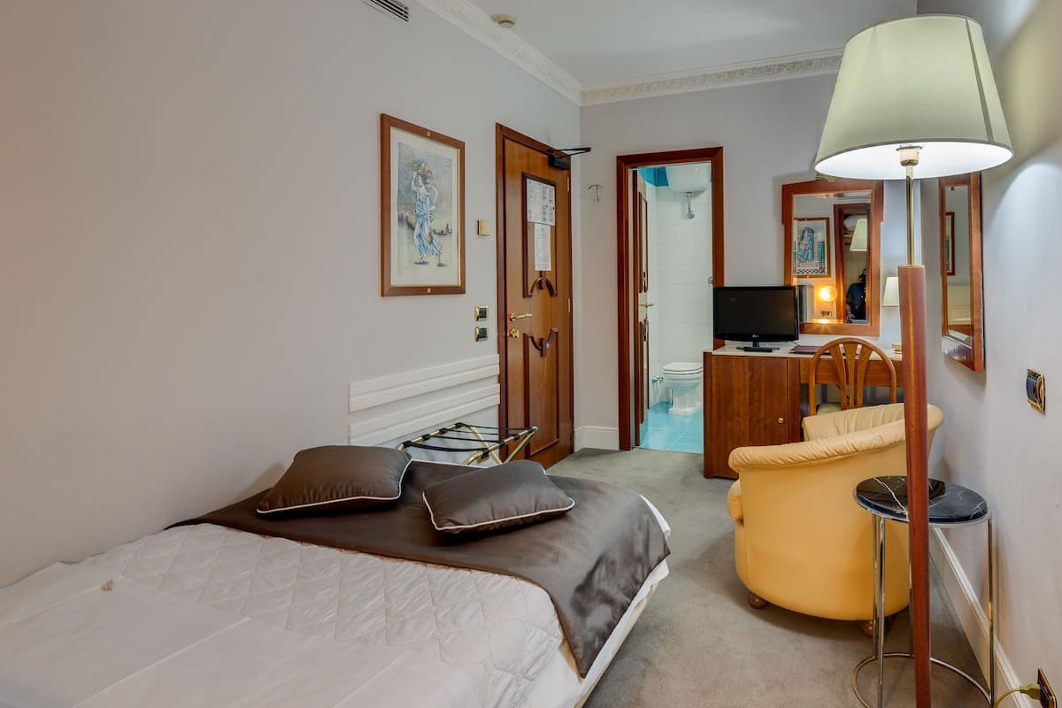 A hotel room with a bed, a desk, a chair, a television, and a lamp.