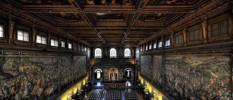 An ornate interior with high ceilings, detailed frescoes, and a central aisle leading to an altar.