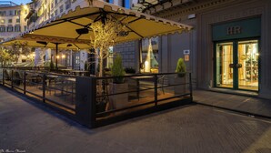 An outdoor café with tables and chairs under a canopy, surrounded by buildings.