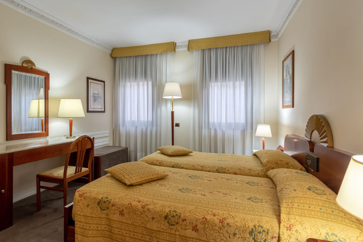 A hotel room with two beds, a desk, a chair, and a large window with curtains.