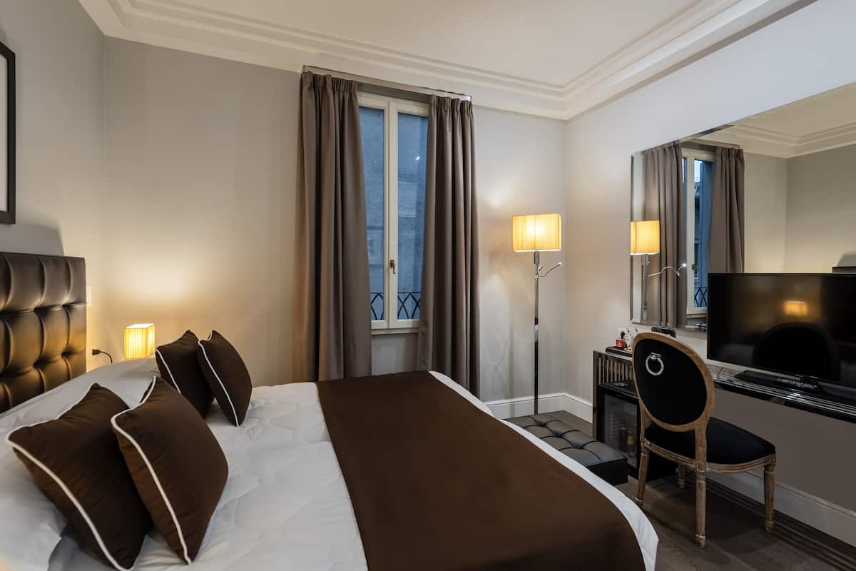 A hotel room with a large bed, a desk with a chair, a television, and a window with curtains.
