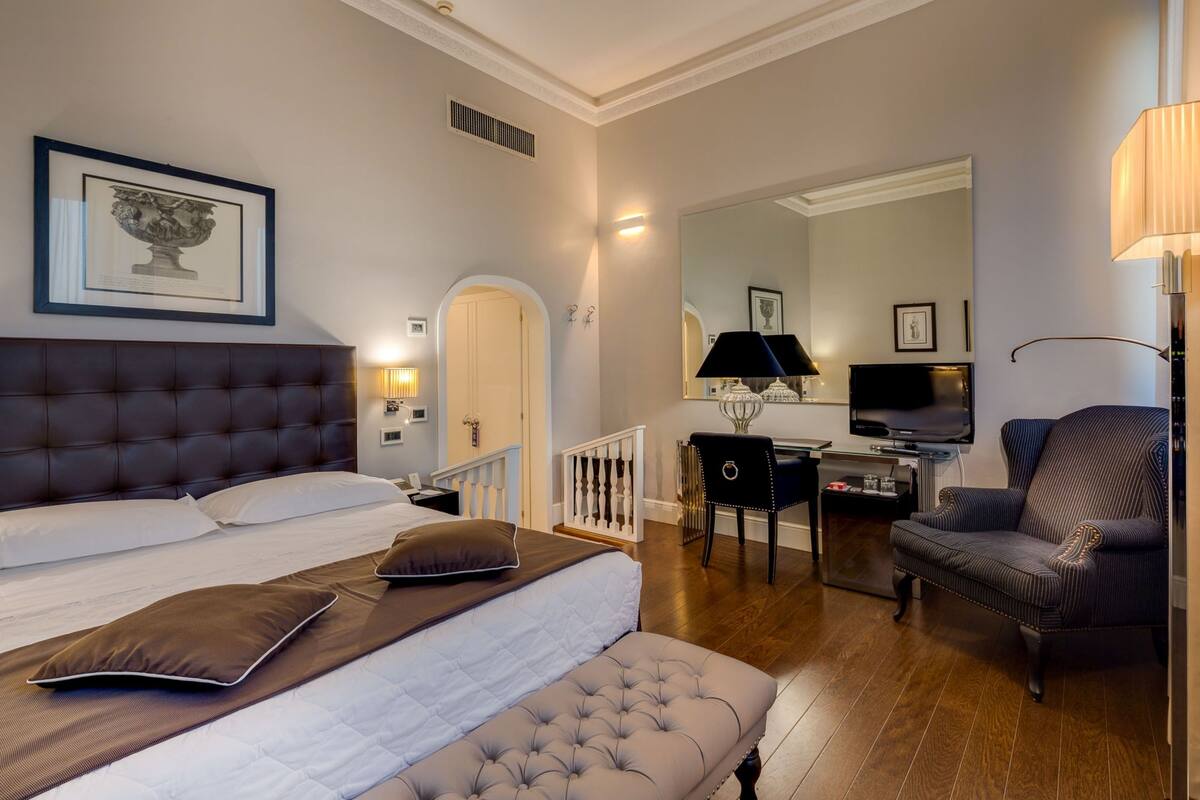 A bedroom with a large bed, a desk with a chair, a television, and a lamp.