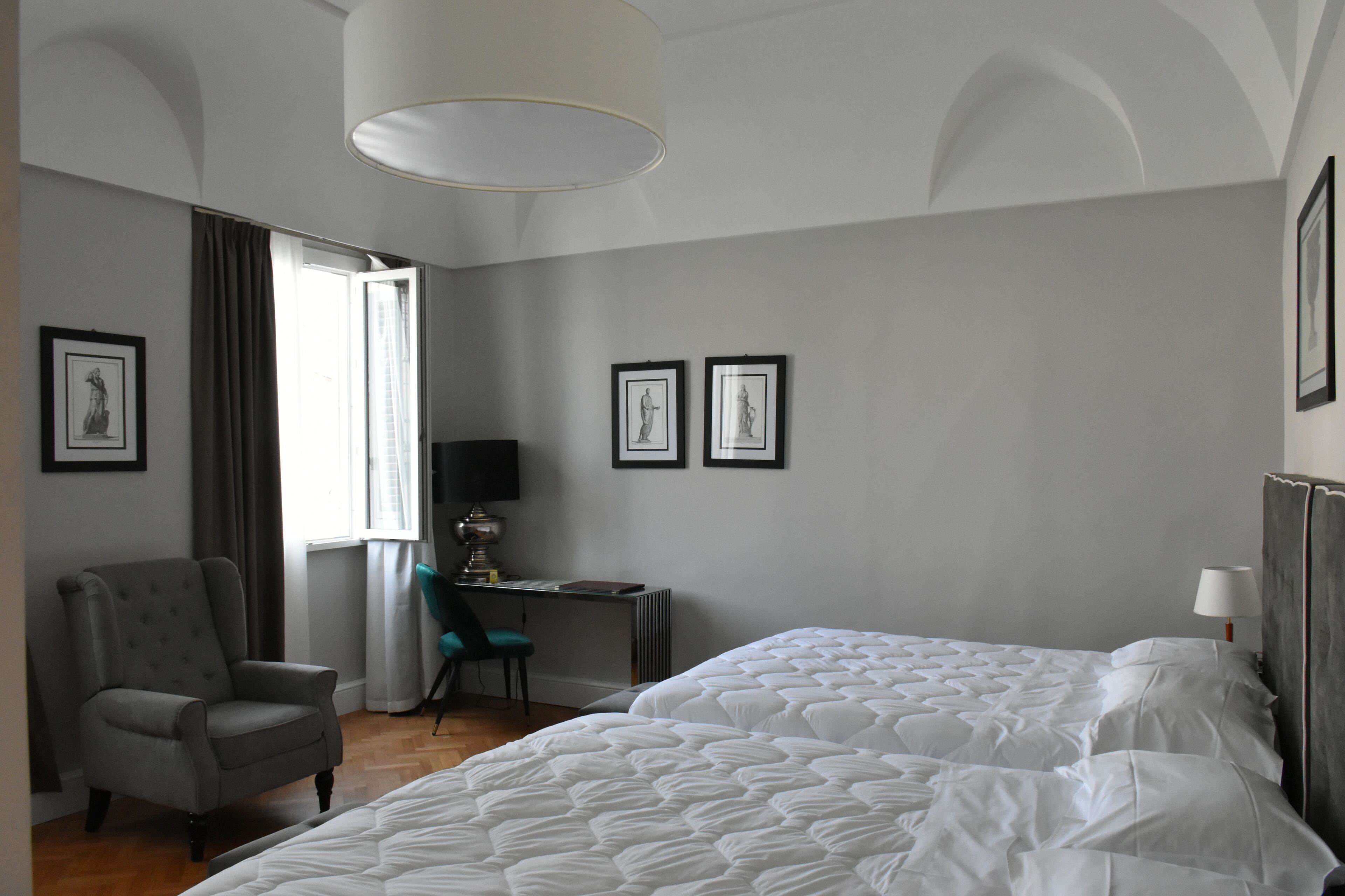 A hotel room with a bed, a desk, a chair, and framed artwork on the walls.