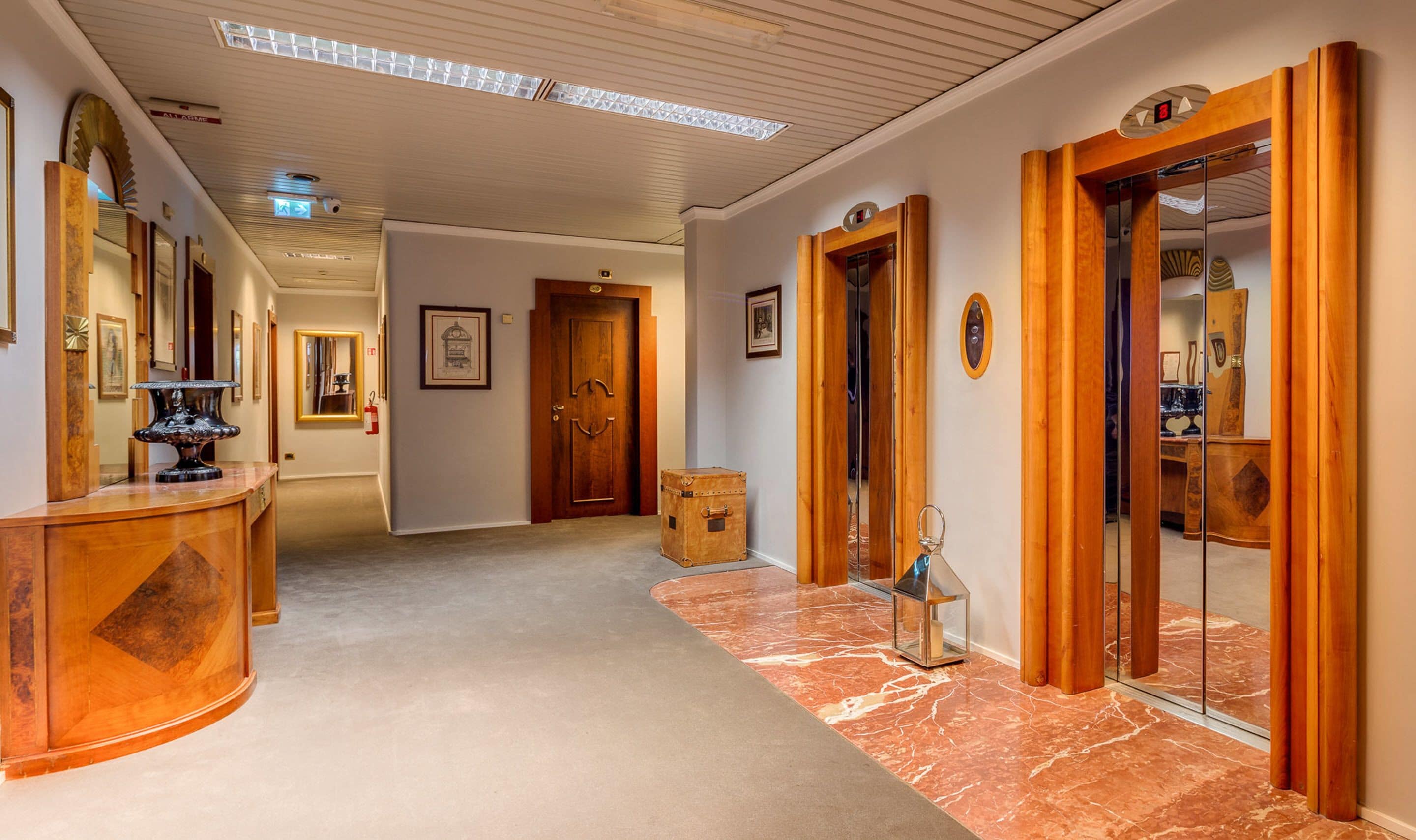 Un couloir d’hôtel avec un sol en marbre, des portes en bois et un comptoir de réception doté d’un miroir.