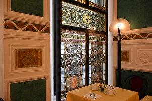 Zona pranzo con tavolo apparecchiato per due, una finestra decorativa in vetro colorato e una parete con pannelli intarsiati.