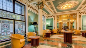 A luxurious lobby with ornate columns, a grand chandelier, and a large mirror reflecting the room.