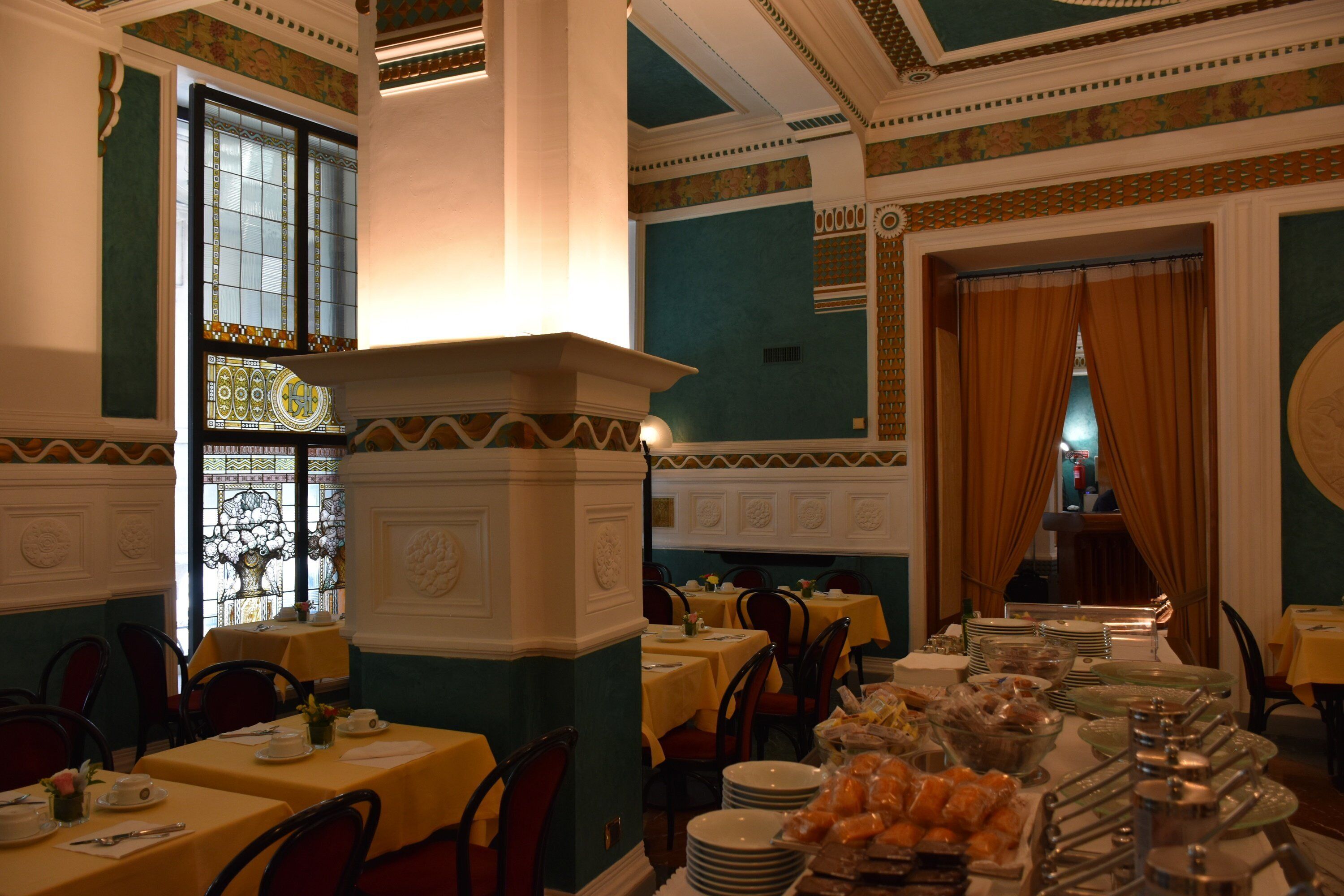 A dining area with tables set for a meal, a large window with decorative glass, and a view of the street outside.