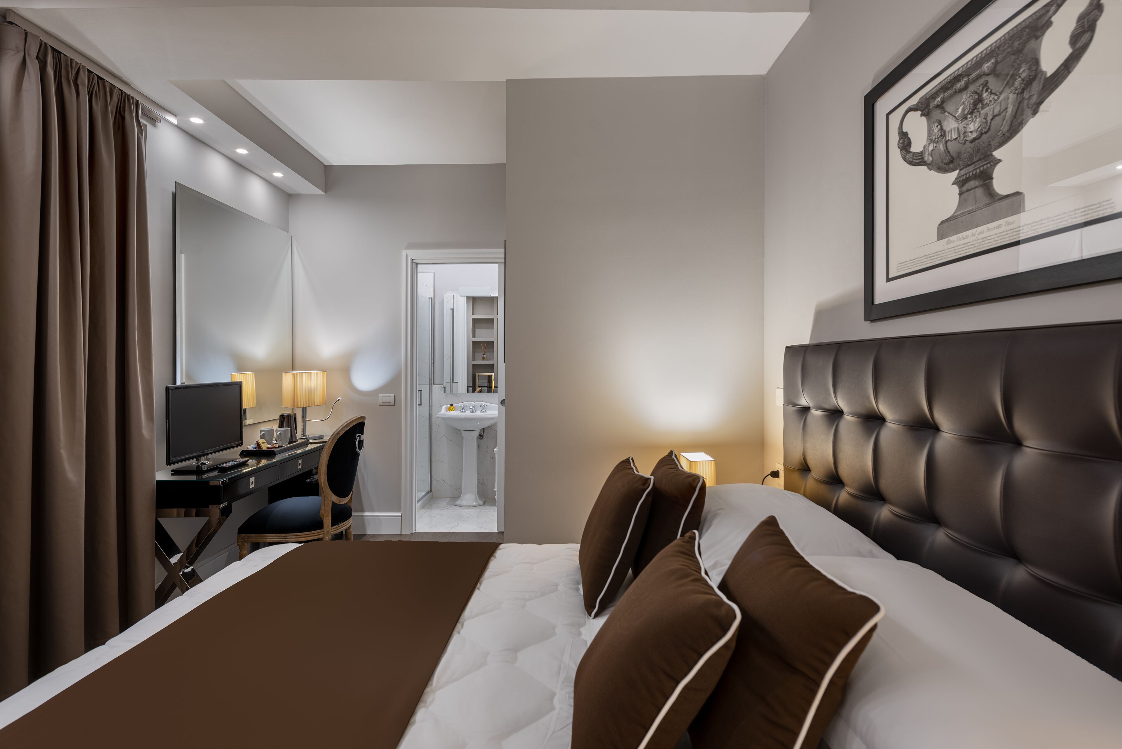 Een moderne hotelkamer met een groot bed, een bureau met een computer, een stoel en een badkamer die door een open deur zichtbaar is.