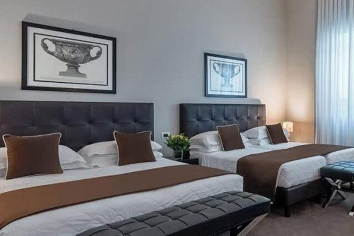A hotel room with two beds, a desk, a chair, and a lamp.