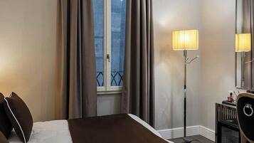 A hotel room with a bed, bedside lamps, a TV, and a window with curtains.