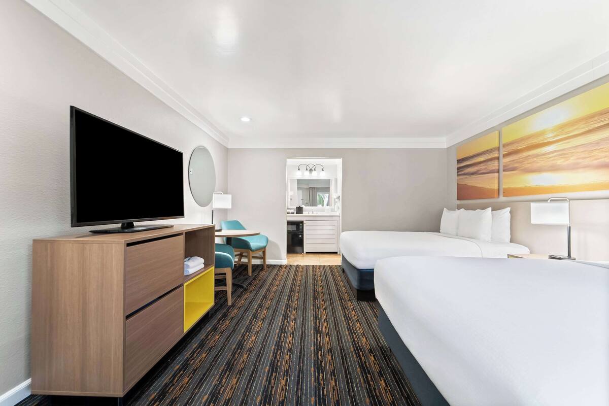 Ein Hotelzimmer mit Flachbildfernseher, Schreibtisch mit Stuhl, Bett, Badezimmer mit Spiegel und Bildern an den Wänden.