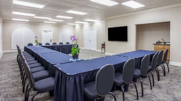 Un salón de conferencias con una larga mesa, sillas, una pantalla de televisión y una pequeña kitchenette.