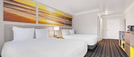 A hotel room with two beds, a large painting on the wall, a carpeted floor, and a small desk with a lamp.